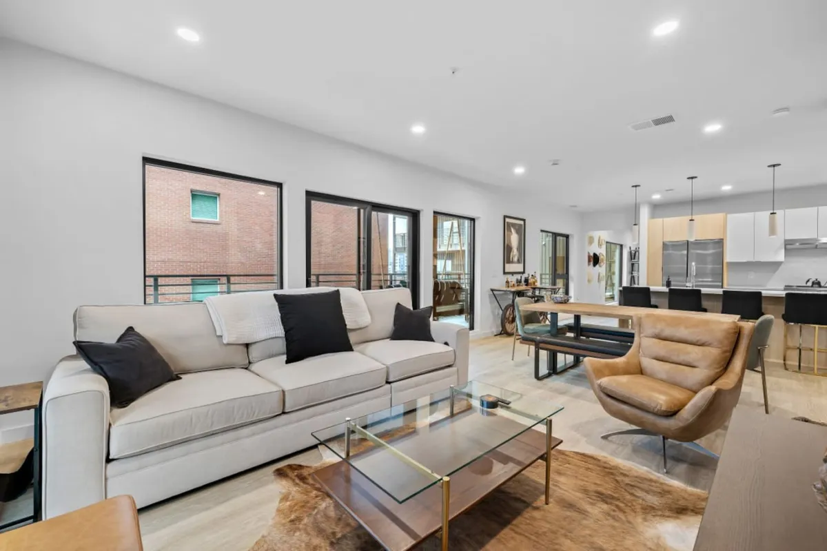 The image showcases a stylish, open-concept living space featuring a plush sofa, sleek glass coffee table, spacious dining area, and a modern kitchen. The ambiance is comfortable yet contemporary, inviting guests to relax, gather, and entertain. The layout easily accommodates social gatherings, family meals, and memorable celebrations, all set against the backdrop of Nashville's vibrant city energy.