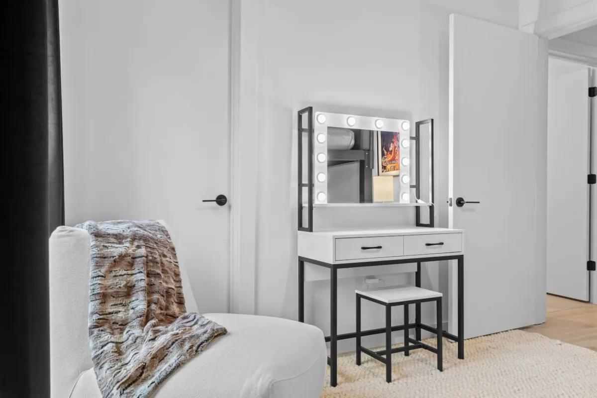 A serene vanity area with a mirror, cozy chair, and decorative throw blanket, exuding a peaceful and chic atmosphere. The design suggests a perfect spot for personal reflection, morning routines, or winding down after an active day.