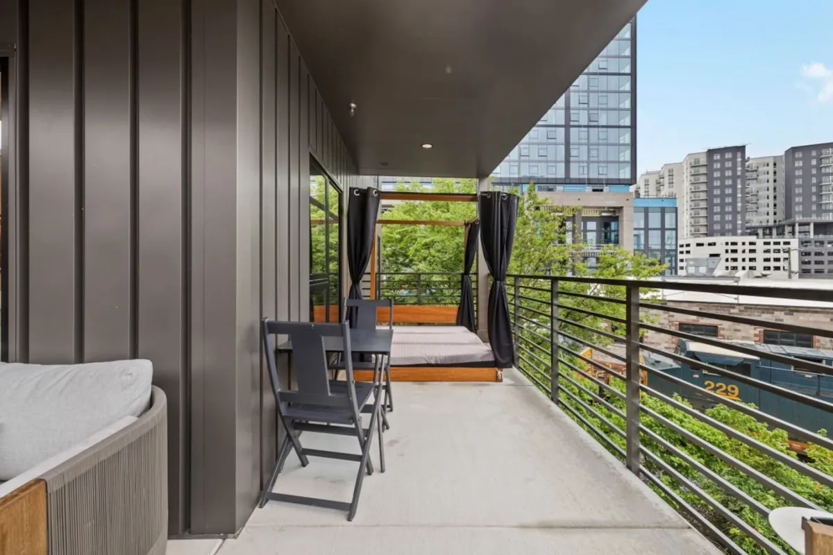 A modern outdoor lounge area overlooking the cityscape, featuring a comfortable sitting area with chairs and an outdoor bed. The view highlights the urban environment and offers a tranquil spot to enjoy sunsets or city lights after a day exploring Nashville.