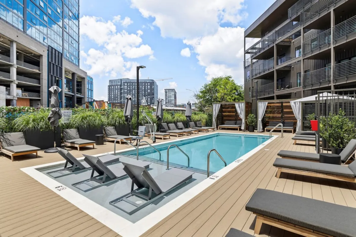 A stylish swimming pool framed by lounging chairs and lush greenery, offering a space for swimming, sunbathing, or enjoying the outdoors. The scene balances leisure with an appreciation for city living and natural elements.