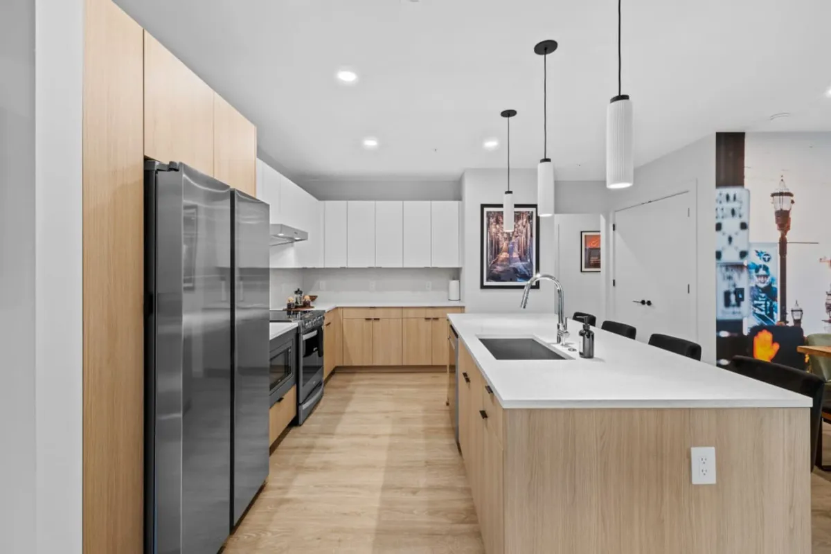 A spacious, modern kitchen is shown with a large kitchen island, stainless steel appliances, pendant lighting, and tasteful wall art. The scene radiates a welcoming, functional vibe, suitable for both casual and gourmet cooking and lively family or group gatherings.