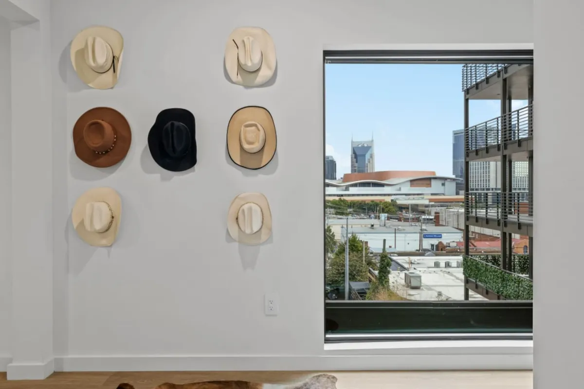 A casually decorated living space with cowboy hats, a large window framing a cityscape, and room for friends to gather. The ambiance is cheerful and social, with the promise of memorable moments set against the Nashville skyline.